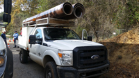 Composite utility poles loaded onto an overhead pickup truck rack for transporting to site